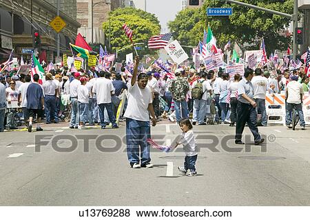Stock Photo - Hispanic girl and father with American flag watch hundreds of thousands of immigrants participating in march for Immigrants and Mexicans protesting against Illegal Immigration reform by U. S. Congress, Los Angeles, CA, May 1, 2006. Fotosearch