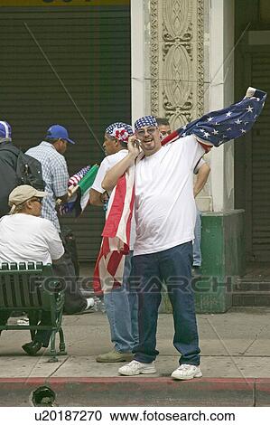 Stock Image - Hispanic man on cellphone with American flag participates in march for Immigrants and Mexicans protesting against Illegal Immigration reform by U. S. Congress, Los Angeles, CA, May 1, 2006. Fotosearch