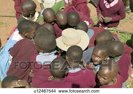 Picture - Karimba School with school children surrounding white man with straw hat on, in North Kenya, Africa. Fotosearch