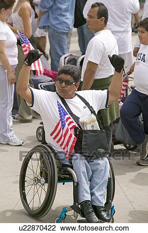 Stock Image - Man in wheel chair holds US flag in sympathy with hundreds of thousands of immigrants participating in march for Immigrants and Mexicans protesting against Illegal Immigration reform by U. S. Congress, Los Angeles, CA, May 1, 2006. Fotosearch