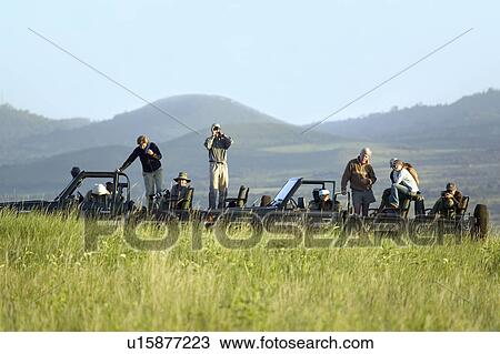Stock Image - Masai scout and tourists look for animals from a Landcruiser during a game drive at the Lewa Wildlife Conservancy in North Kenya, Africa. Fotosearch