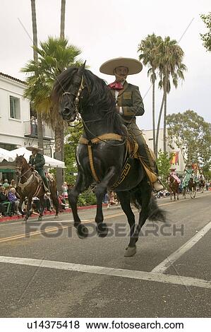 Stock Photo - Mexican horseback riders trot along during the opening day parade down State Street of Old Spanish Days Fiesta held every August in Santa Barbara, California. Fotosearch
