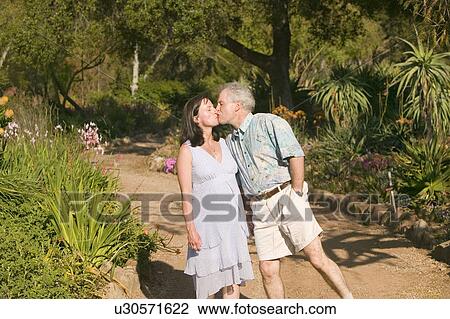 Stock Image - Middle-aged husband walks down springtime path with his pregnant wife in gardens in Ojai, California. Fotosearch