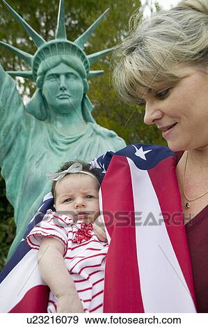 Stock Photo - Mother and newborn baby (Sophia Larson) wrapped in American flag stand in front of a Statue of Liberty, was born on October 16th, the birthday of the 300 Millionth American, Ventura, California. Fotosearch