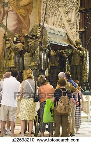 Stock Image - Tourists look at the mausoleum-monument and ornate tomb of Christopher Columbus where four heralds dressed in full court mourning carry the sarcophagus; they bear respectively the arms of, Castile, Léon, Aragon, and Navarre, the four nations which united . Fotosearch
