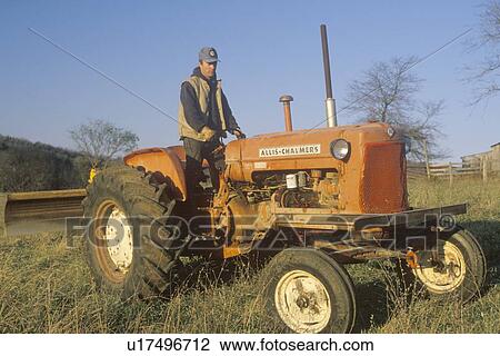 Stock Image - Farmer standing on tractor on cattle farm in Bourbon, MO. Fotosearch