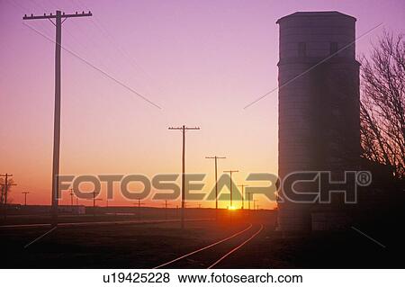 Stock Photo - Sunset silhouette of grain silo beside train tracks. Fotosearch
