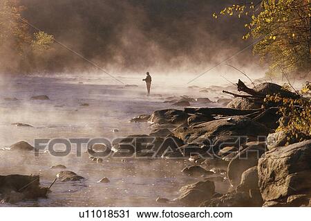 Stock Image - Solitary fly fisherman in morning mist. Fotosearch