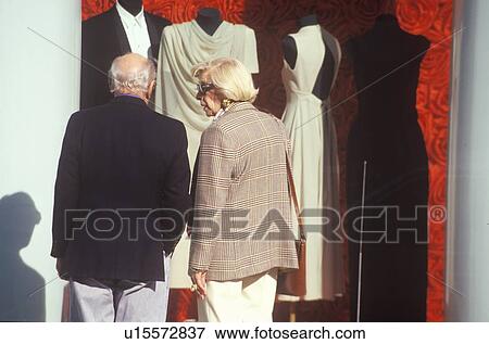 Shoppers looking at gowns and tuxedos in storefront window View Large Photo Image Stock Photo - Shoppers looking at gowns and tuxedos in storefront window. Fotosearch
