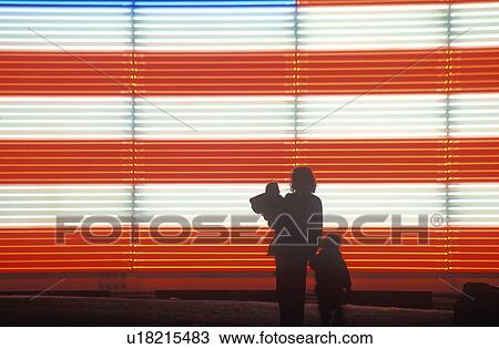 Stock Image - Silhouetted family in front of an American electric Flag. Fotosearch