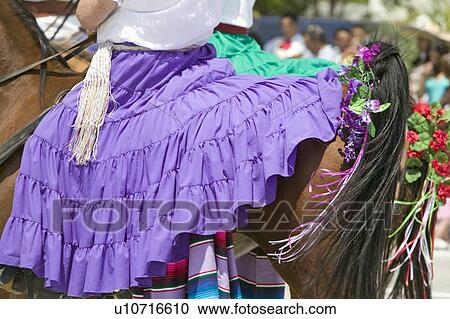 Stock Image - Woman with Spanish purple dress riding horse during opening day parade. Fotosearch