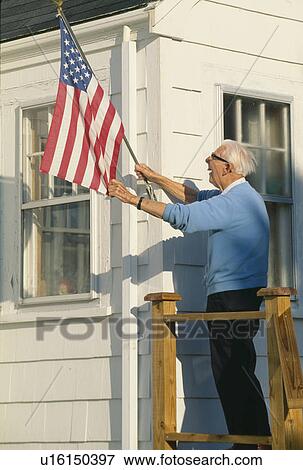 Stock Photo - Senior citizen raising the American flag on house. Fotosearch