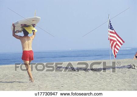 Lifeguard walking past an American flag planted in the sand View Large Photo Image Stock Photo - Lifeguard walking past an American flag planted in the sand. Fotosearch