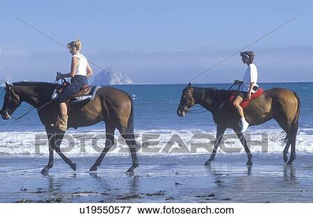 Stock Photo - Pair of girls on horseback on beach. Fotosearch