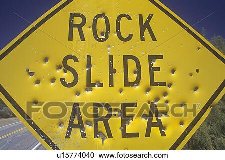 Stock Image - Bullet holes in a “Rock Slide Area” sign, Southern California. Fotosearch