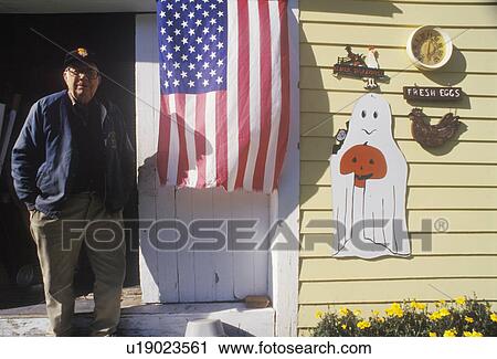 Stock Image - Man Standing by American Flag Hung on His Home. Fotosearch