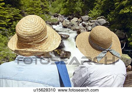 Stock Image - Twin straw hats, two women enjoy creek. Fotosearch