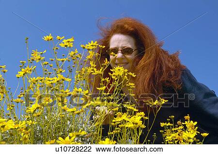 Stock Image - Woman with red hair, May Palmer, smelling yellow flowers. Fotosearch