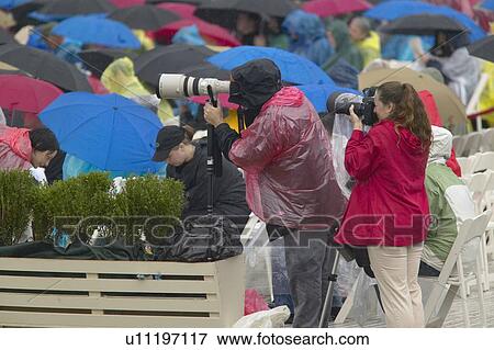 Stock Photo - Guests hold umbrellas in the rain as two photographers record the official opening ceremony of the Clinton Presidential Library. Fotosearch