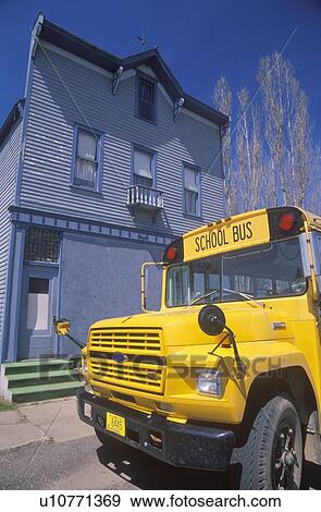 Stock Photo - A yellow schoolbus outside of a wooden frame building. Fotosearch