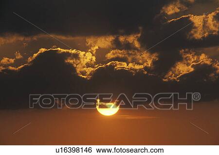 Stock Photograph - Sun Setting Through Clouds. Fotosearch