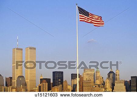 Stock Image - American Flag flying over skyline of New York City from New York Harbor. Fotosearch