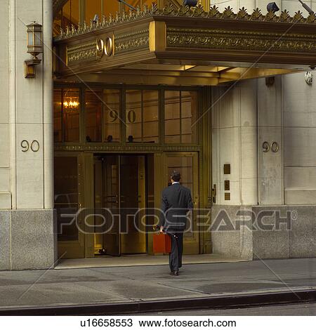 Stock Image - Business man carrying a brief case entering a building, New York City. Fotosearch