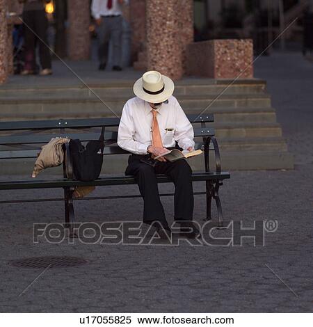 Stock Photography - Man in a white hat sitting on a bench along the esplanade at Battery Park, New York City. Fotosearch
