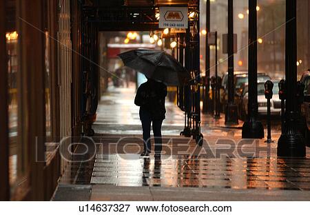 Rear view of person with an umbrella walking on the sidewalk View Large Photo Image Stock Photo - Rear view of person with an umbrella walking on the sidewalk. Fotosearch