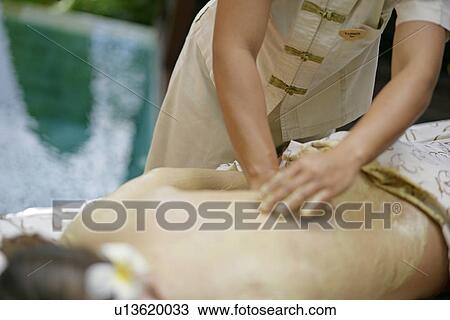 Stock Image - A person massaging cream on a woman’s back.. Fotosearch