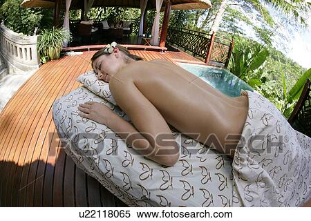 Stock Photography - A young topless woman lying on a table with eyes closed.. Fotosearch