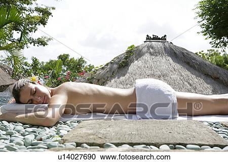 Stock Image - A young woman lying on stony ground for sun bathing.. Fotosearch