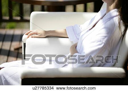 Picture - Midsection of young woman sitting on a chair.. Fotosearch