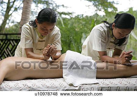 Stock Photo - Two masseuses massaging a woman’s body.. Fotosearch