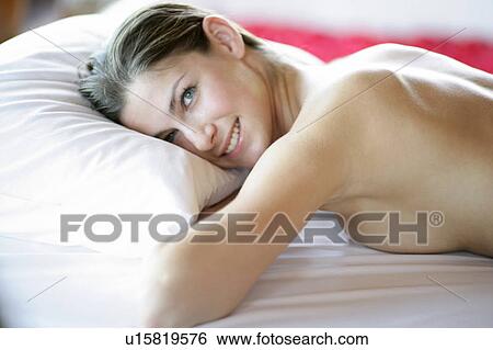 Stock Photograph - A topless young woman lying on bed with toothy smile.. Fotosearch
