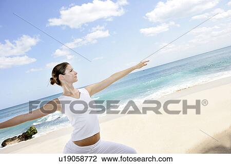 Stock Image - A woman exercising on a beach with arms out.. Fotosearch
