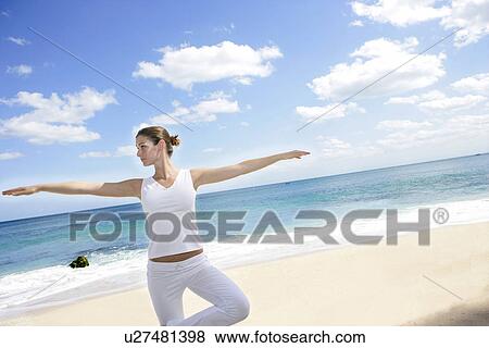 Stock Photo - A woman exercising on a beach with arms out.. Fotosearch