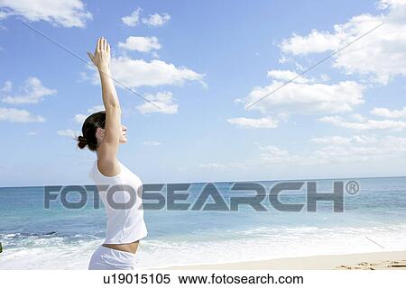 Stock Photography - A woman exercising on a beach with hands raised.. Fotosearch