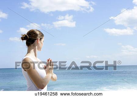 Stock Photo - A woman meditating on a beach with joined hands.. Fotosearch