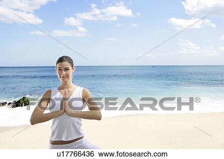 Stock Photograph - A woman meditating on a beach with joined hands.. Fotosearch