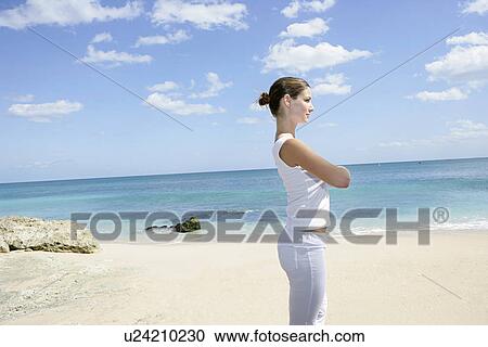 Stock Image - A woman standing on a beach with hands folded.. Fotosearch
