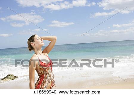 Stock Image - A young woman standing along seashore.. Fotosearch