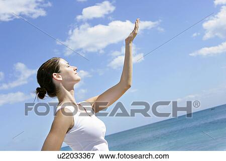 Stock Photo - View of a woman on a beach with arm raised.. Fotosearch