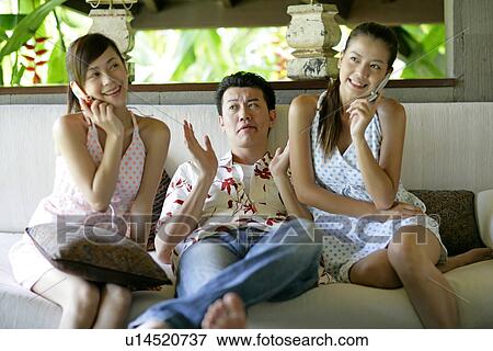 Stock Photo - Women on phone and man sitting in between.. Fotosearch