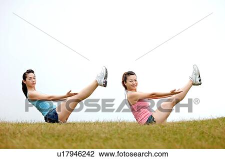 Stock Image - View of young women exercising on grassland.. Fotosearch