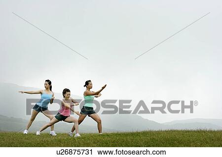 Stock Image - View of young women exercising on grassland.. Fotosearch