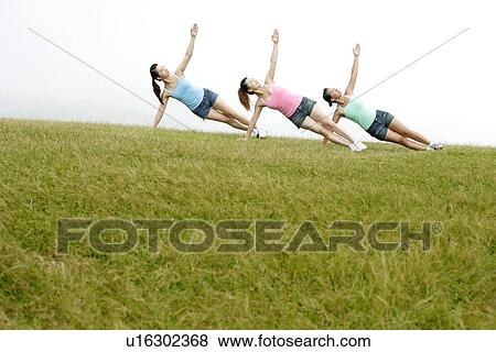 Stock Photo - View of young women exercising on grassland.. Fotosearch