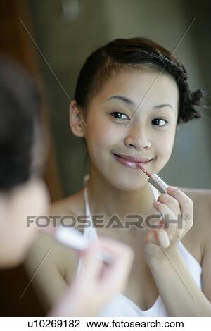 Stock Image - Woman applying a lipstick on her lips.. Fotosearch