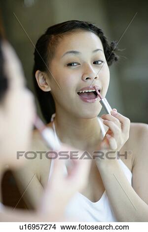 Picture - Woman applying lipstick on her lips.. Fotosearch
