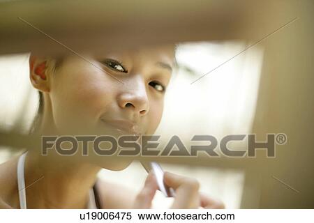 Stock Photography - Blurred view of a young woman applying a lipstick.. Fotosearch